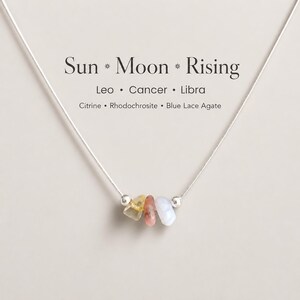 May include: A delicate silver necklace with three small gemstones: yellow citrine, pink rhodochrosite, and pale blue lace agate. The necklace is inscribed with "Sun * Moon * Rising" and the zodiac signs Leo, Cancer, and Libra.