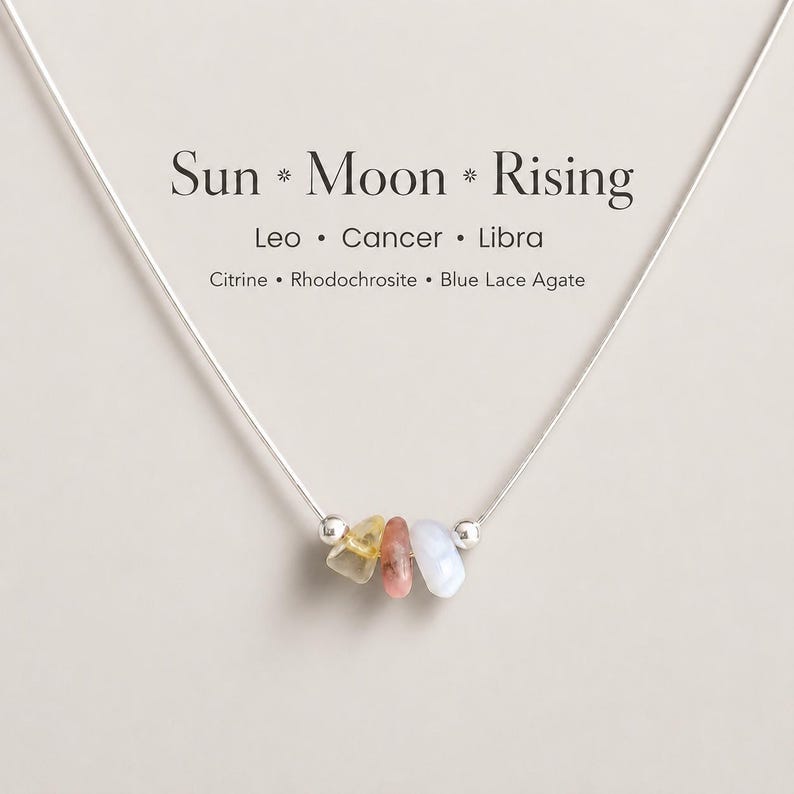 May include: A delicate silver necklace with three small gemstones: yellow citrine, pink rhodochrosite, and pale blue lace agate. The necklace is inscribed with "Sun * Moon * Rising" and the zodiac signs Leo, Cancer, and Libra.