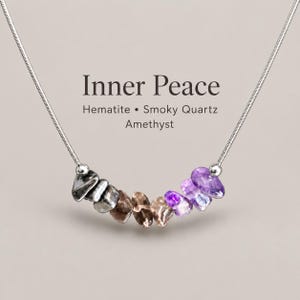 May include: A silver-toned snake chain necklace featuring a row of tumbled gemstone beads in shades of metallic gray, brown, and purple. The text Inner Peace, Hematite, Smoky Quartz, and Amethyst is printed above the stones.