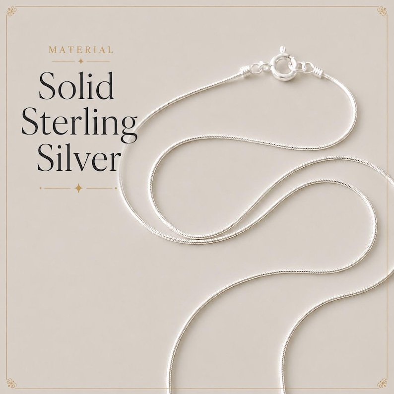 May include: A thin, flexible silver snake chain necklace featuring a circular spring ring clasp. The text on the left side reads: MATERIAL Solid Sterling Silver. The chain is arranged in a curved, looping pattern against a neutral background.
