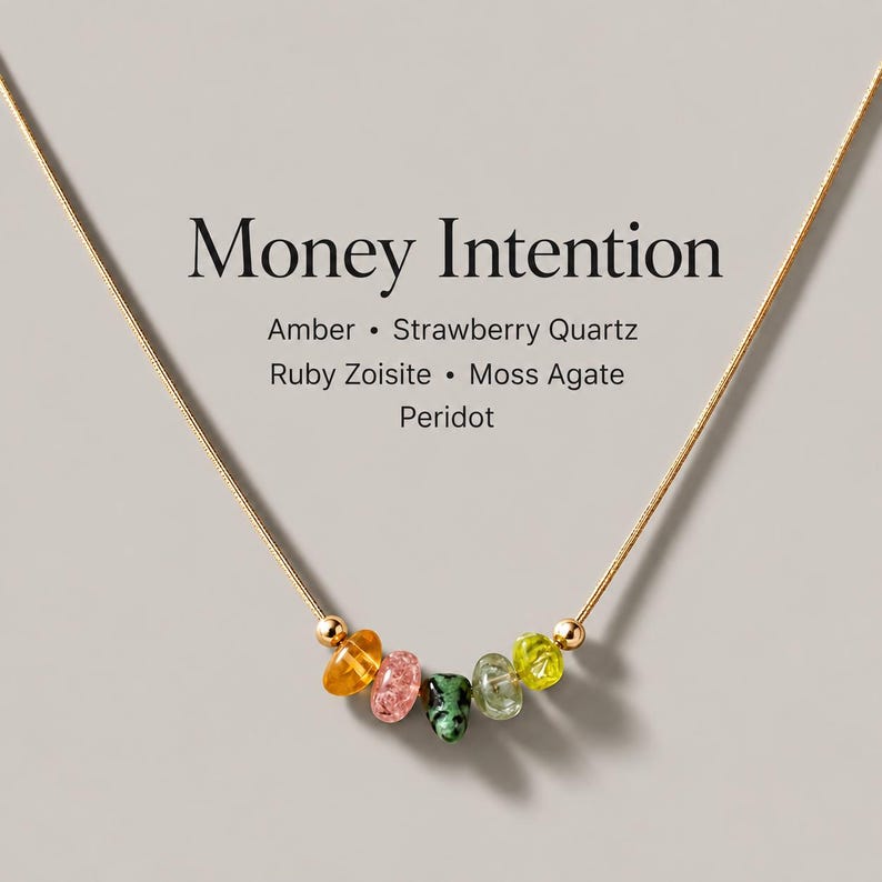 May include: A gold-toned chain necklace featuring five small, irregular tumbled gemstones in amber, strawberry quartz, ruby zoisite, moss agate, and peridot. The text reads Money Intention, Amber, Strawberry Quartz, Ruby Zoisite, Moss Agate, Peridot.