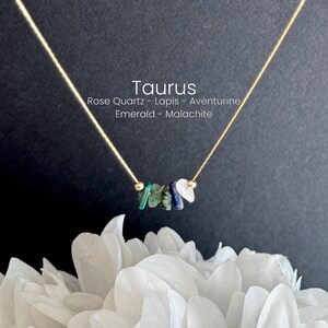 K&ouml;nnte beinhalten: Eine zarte Halskette mit einer d&uuml;nnen goldfarbenen Kette und einer Ansammlung kleiner, unregelm&auml;&szlig;iger Edelstein-Splitter in Gr&uuml;n, Blau und Wei&szlig;. Der Text Taurus, Rose Quartz, Lapis, Aventurine, Emerald, Malachite ist sichtbar.