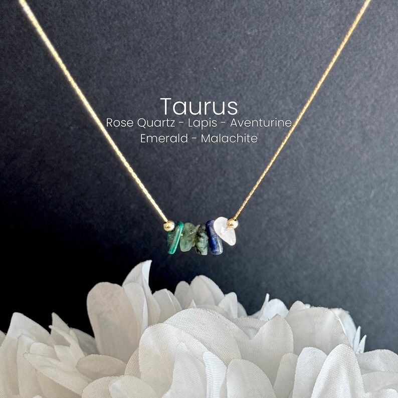 K&ouml;nnte beinhalten: Eine zarte Halskette mit einer d&uuml;nnen goldfarbenen Kette und einer Ansammlung kleiner, unregelm&auml;&szlig;iger Edelstein-Splitter in Gr&uuml;n, Blau und Wei&szlig;. Der Text Taurus, Rose Quartz, Lapis, Aventurine, Emerald, Malachite ist sichtbar.