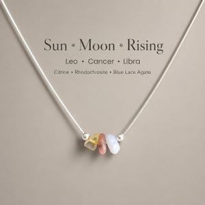 May include: A silver necklace with three gemstones: citrine, rhodochrosite, and blue lace agate. The necklace has the text "Sun * Moon * Rising" and the zodiac signs Leo, Cancer, and Libra.