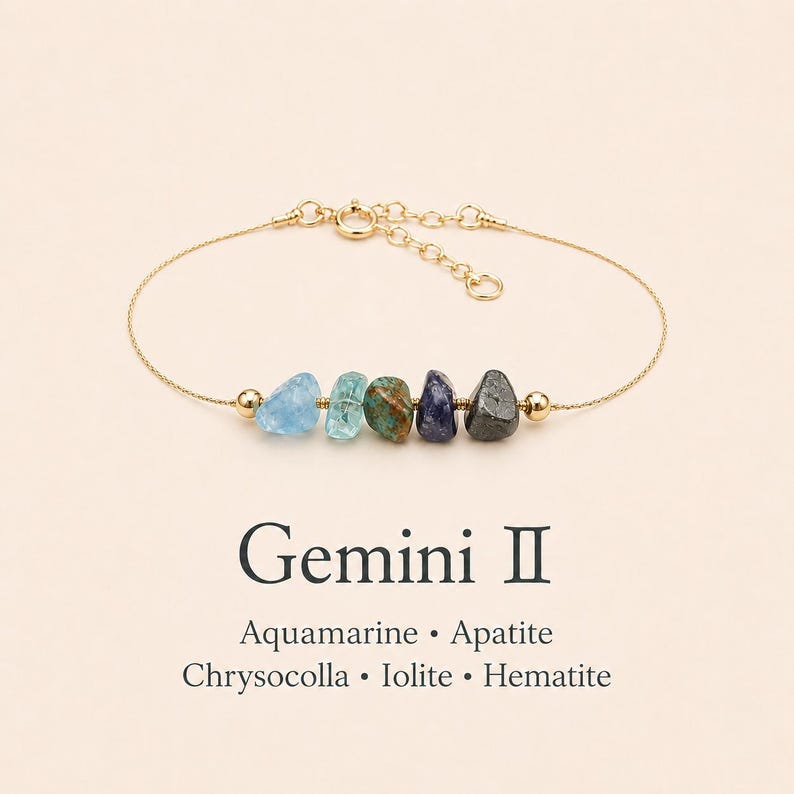 May include: A gold-colored chain bracelet featuring five colorful gemstone beads: aquamarine, apatite, chrysocolla, iolite, and hematite. The text "Gemini II" and the names of the gemstones are below the bracelet.