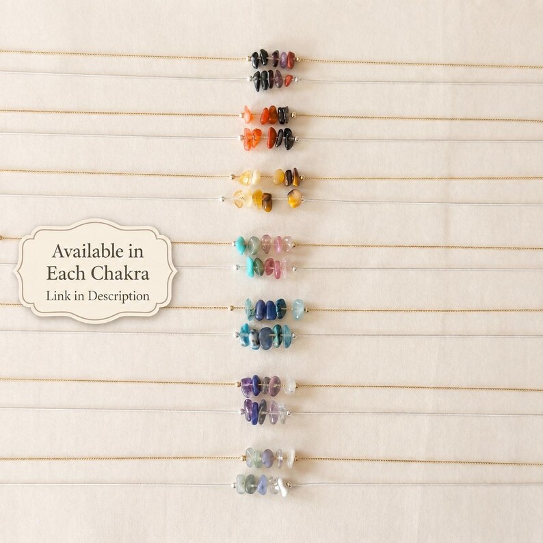 May include: A selection of necklaces, each with a fine gold chain and a row of small, colourful gemstones. The gemstones are in various colours, including black, orange, yellow, blue, and purple. The text "Available in Each Chakra, Link in Description" is also visible.