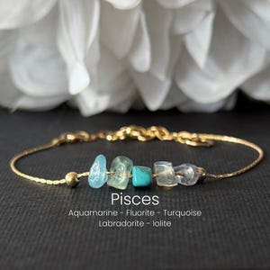 May include: A gold-colored chain bracelet featuring a series of colorful gemstones. The bracelet includes blue, green, and clear stones. The word "Pisces" is displayed below the stones, along with the names of the gemstones.