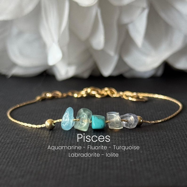 May include: A gold-colored chain bracelet featuring a series of colorful gemstones. The bracelet includes blue, green, and clear stones. The word "Pisces" is displayed below the stones, along with the names of the gemstones.