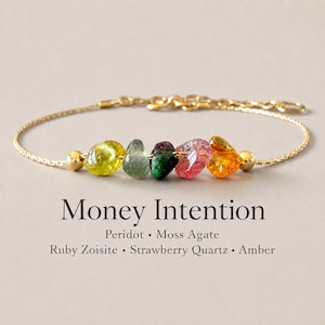 May include: A gold chain bracelet featuring five raw, multi-colored gemstone beads including peridot, moss agate, ruby zoisite, strawberry quartz, and amber. Text below reads: Money Intention, Peridot, Moss Agate, Ruby Zoisite, Strawberry Quartz, Amber.