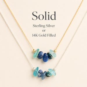 May include: Two necklaces with blue gemstone pendants. One necklace is gold-colored, the other is silver-colored. The text "Solid" and "Sterling Silver or 14K Gold Filled" are displayed above the necklaces.