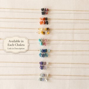 Pu&ograve; includere: Una collezione di delicate collane, ognuna con una fila di piccole pietre preziose colorate. Le pietre preziose sono disposte in fila, con una variet&agrave; di colori tra cui nero, arancione, giallo, blu e viola. Il testo "Available in Each Chakra, Link in Description" &egrave; visibile.