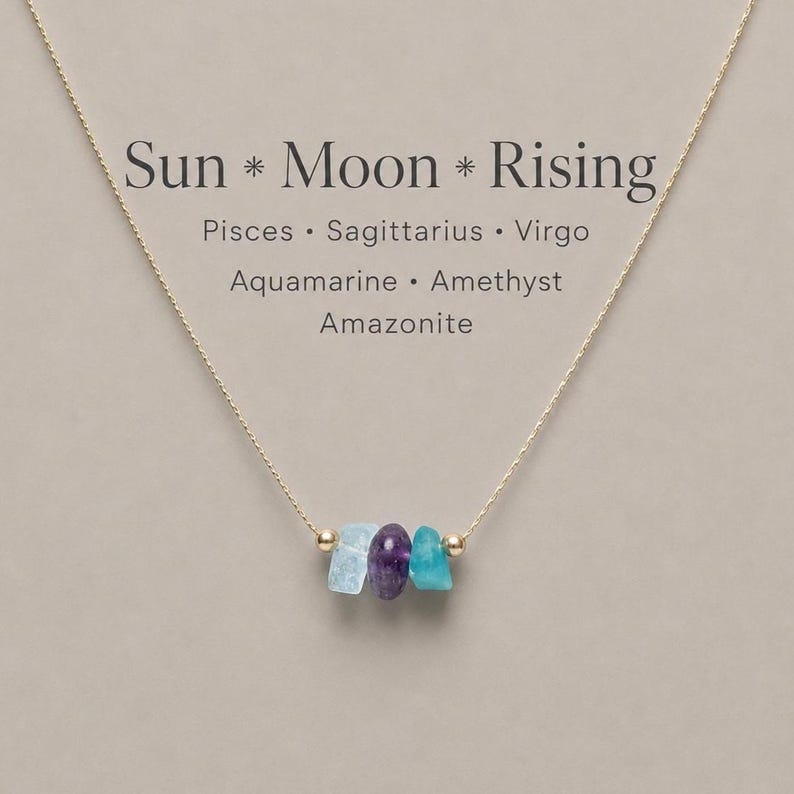 May include: A gold-coloured necklace with three raw gemstones: aquamarine, amethyst, and amazonite. The necklace has the text "Sun * Moon * Rising". The gemstones are light blue, purple, and teal. The chain is delicate and fine.