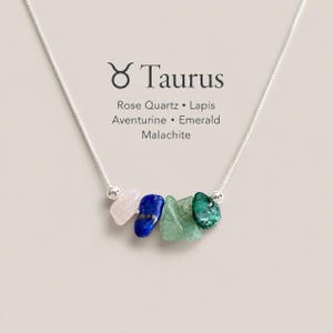K&ouml;nnte beinhalten: Eine silberne Halskette mit f&uuml;nf rohen, getrommelten Edelsteinperlen in den Farben Hellrosa, Tiefblau, Hellgr&uuml;n und Dunkelgr&uuml;n. Der Text Taurus, Rose Quartz, Lapis, Aventurine, Emerald, Malachite ist &uuml;ber den Steinen aufgedruckt.