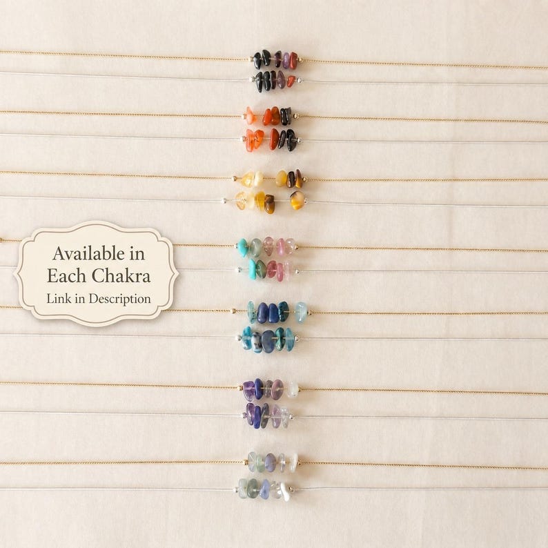 May include: A collection of delicate necklaces, each featuring a strand of small, colorful gemstones. The gemstones are arranged in a row, with a variety of colors including black, orange, yellow, blue, and purple. The text "Available in Each Chakra, Link in Description" is also visible.