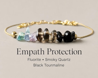 May include: A gold-toned chain bracelet featuring a row of raw, tumbled gemstones including green and blue fluorite, light purple amethyst, brown smoky quartz, and black tourmaline, with text reading Empath Protection Fluorite Smoky Quartz Black Tourmaline.