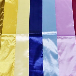 May include: A collection of colorful satin ribbons in various shades, including green, gold, yellow, blue, light blue, lavender, magenta, and pink. The ribbons are arranged side by side, showcasing their glossy texture.