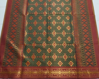 May include: A green and gold patterned fabric with a red border. The fabric has a geometric design with small diamonds and squares.