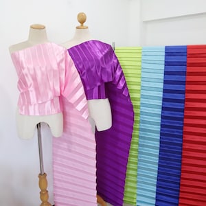 May include: Assortment of pleated fabric in various colors, including pink, purple, green, blue, and red. The fabric is displayed on a white background and is arranged in a vertical row.