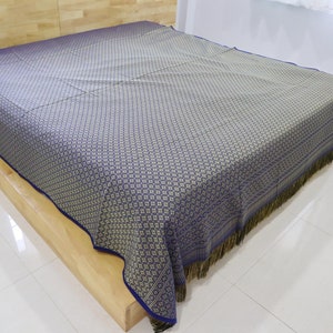 May include: A blue and gold patterned bedspread with a fringe border. The bedspread is made of a soft, woven fabric and has a subtle sheen.