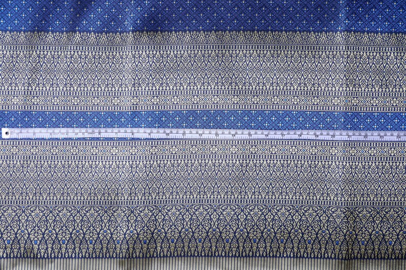 May include: A close-up of a blue and white patterned fabric with a white measuring tape across the middle. The fabric has a repeating pattern of small white flowers and a larger pattern of white flowers and leaves.