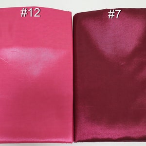 May include: Two folded fabric samples, one in a vibrant fuchsia pink labeled "#12" and the other in a deep burgundy labeled "#7". The fabrics have a smooth, shiny texture, suggesting a satin or silk material.