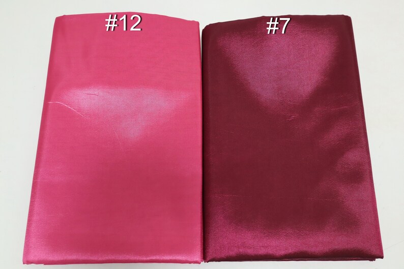 May include: Two folded fabric samples, one in a vibrant fuchsia pink labeled "#12" and the other in a deep burgundy labeled "#7". The fabrics have a smooth, shiny texture, suggesting a satin or silk material.