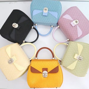 May include: Six different colored handbags with a unique woven design and a silver clasp. The handbags are arranged in a circle with the handles facing outwards.