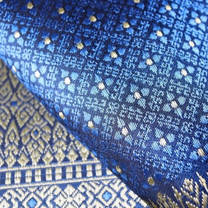 May include: Close-up of blue and gold patterned fabric with a repeating geometric design. The fabric is woven with a subtle sheen and has a luxurious feel.