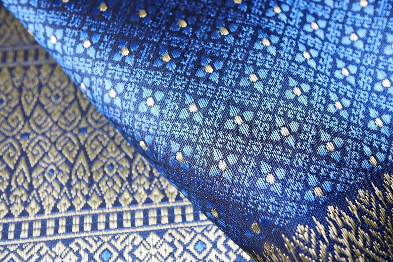 May include: Close-up of blue and gold patterned fabric with a repeating geometric design. The fabric is woven with a subtle sheen and has a luxurious feel.
