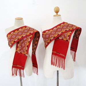 May include: Two red sashes with embroidered patterns and fringe. The sashes are displayed on mannequins.