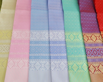 May include: A collection of eight different patterned fabrics in various colours, including green, beige, pink, blue, turquoise, purple, and red. The fabrics have a woven texture and feature intricate geometric designs.