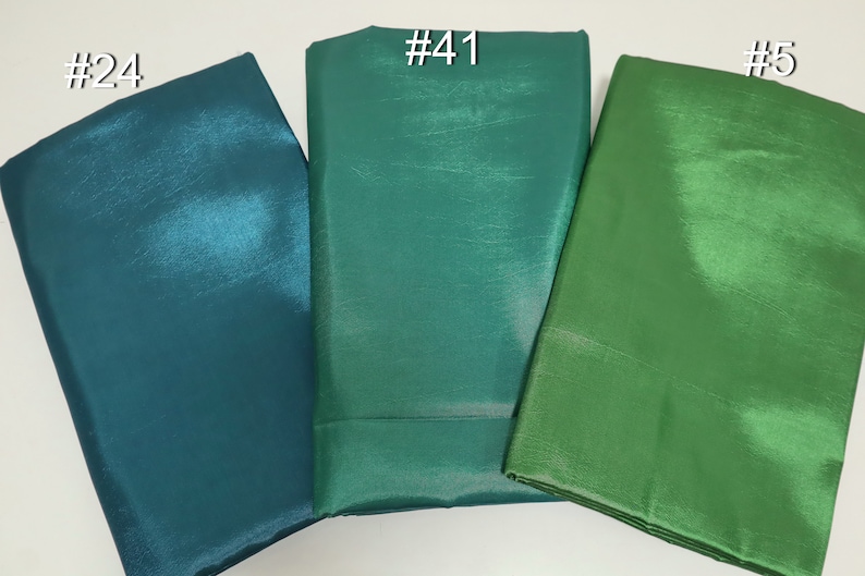 May include: Three folded fabric swatches in shades of green and teal. The swatches are labeled with white numbers: #24, #41, and #5. The fabric has a shiny, textured appearance.