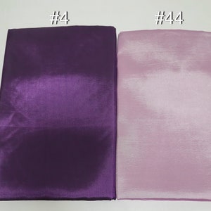 May include: Two folded fabric samples, one deep purple and the other a light lavender. The fabric has a shiny, satin-like appearance. The top left corner of the purple fabric has the text "#4" and the top right corner of the lavender fabric has the text "#44".