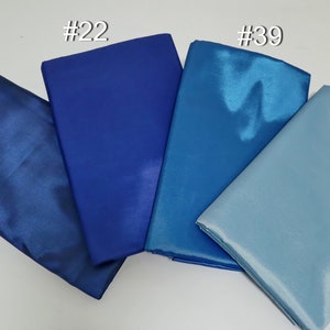 May include: Four folded fabric samples in shades of blue, from deep navy to light sky blue. The fabrics have a shiny, satin-like finish. Each sample is labeled with a number in white.