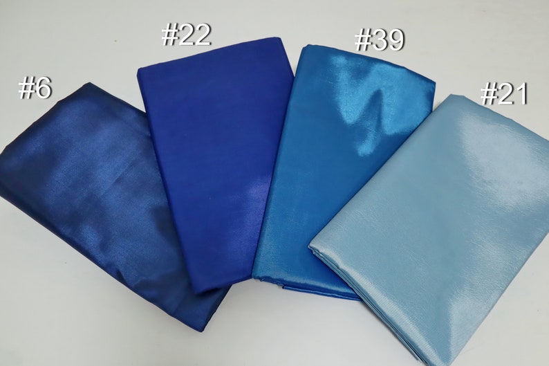 May include: Four folded fabric samples in shades of blue, from deep navy to light sky blue. The fabrics have a shiny, satin-like finish. Each sample is labeled with a number in white.