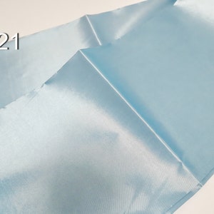 May include: Light blue satin fabric with a shiny finish. The fabric is folded, showing the texture and sheen of the material. The number "#21" is printed in the upper left corner.