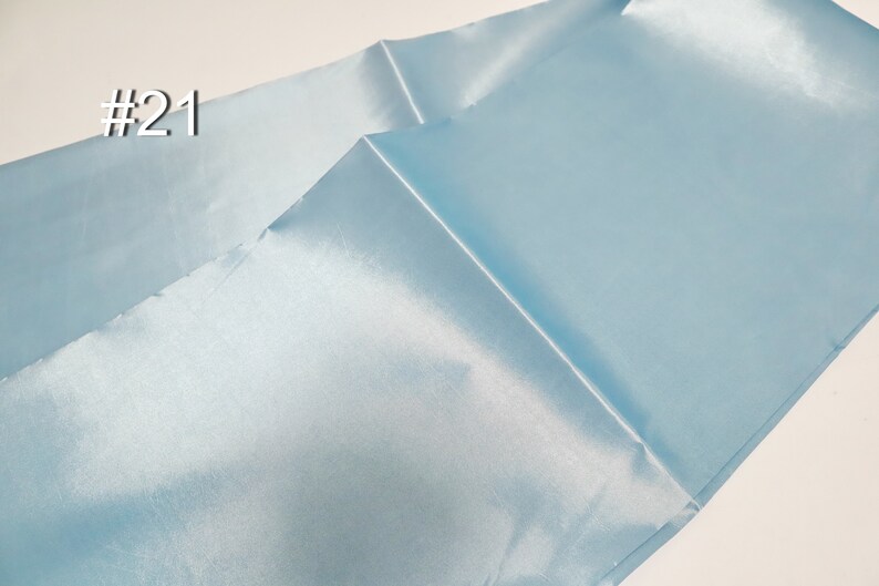 May include: Light blue satin fabric with a shiny finish. The fabric is folded, showing the texture and sheen of the material. The number "#21" is printed in the upper left corner.
