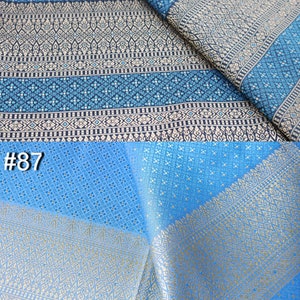 May include: Two pieces of blue fabric with gold and white patterns. The top piece is a darker blue with a more intricate pattern. The bottom piece is a lighter blue with a simpler pattern. The fabric is labeled #8 and #87.