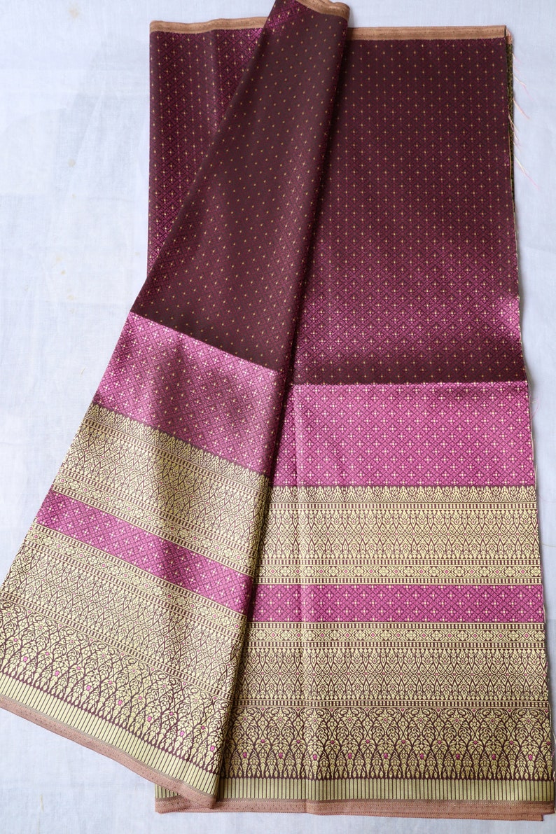 May include: A folded piece of fabric with a brown and pink patterned design. The fabric has a gradient of color from brown to pink. The fabric has a gold trim.