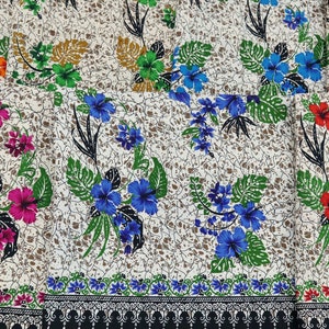 May include: Fabric with a floral pattern featuring hibiscus and other flowers in shades of pink, blue, red, and green. The flowers are set against a cream-colored background with a brown, textured design. A black and white border is at the bottom.