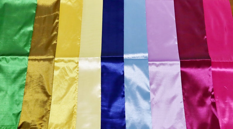 May include: A collection of colorful satin ribbons in various shades, including green, gold, yellow, blue, light blue, lavender, magenta, and pink. The ribbons are arranged side by side, showcasing their glossy texture.