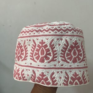 Puede incluir: Una gorra blanca bordada con un diseño floral rosa. La gorra tiene una corona redonda y una visera plana.