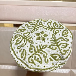 Puede incluir: Gorra blanca con bordados verdes. El diseño presenta un patrón floral detallado en la parte superior y un borde bordado verde. Es un estilo tradicional, con la parte superior redondeada y un borde detallado.