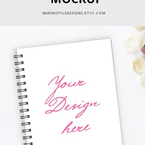 K&ouml;nnte beinhalten: Wei&szlig;es Spiralnotizbuch-Mockup mit dem Text "Spiral Notebook Mockup" und "Your Design here" in Pink. Das Notizbuch ist im A4-Format (21 x 29,7 cm) und hat eine schwarze Spiralbindung. Eine schwarze B&uuml;roklammer befindet sich in der unteren linken Ecke.