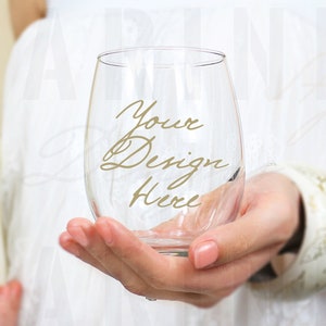 May include: A clear glass stemless wine glass with the text "Your Design Here" written in gold lettering.