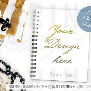 May include: A white spiral-bound notebook with the text "Your Design here" in gold script. A black and gold pen rests beside the notebook. The notebook is 21.6 x 27.9 cm (A4). Other items include gold and white striped fabric, and black jewelry.