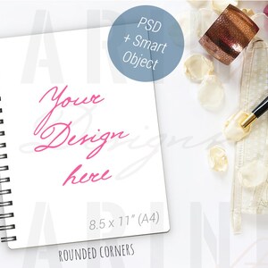 K&ouml;nnte beinhalten: Wei&szlig;es Spiralnotizbuch mit dem Text "Your Design here" in rosa Schrift. Das Notizbuch ist 21,6 x 27,9 cm (A4) gro&szlig; und hat abgerundete Ecken. Ein schwarzer Stift, dekorative Elemente und eine B&uuml;roklammer sind ebenfalls sichtbar.