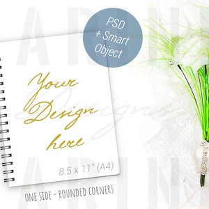 May include: A white spiral-bound notebook with the text "Your Design here" in gold script. The notebook is 8.5 x 11 inches (A4) with rounded corners. A bouquet of white flowers with green stems and accents is to the right.