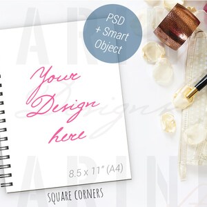 K&ouml;nnte beinhalten: Ein wei&szlig;es Spiralnotizbuch mit dem Text "Your Design here" in rosa Schrift. Das Notizbuch ist 21,6 x 27,9 cm (A4) gro&szlig; und hat quadratische Ecken. Ein schwarzer Stift, eine dekorative Manschette und Bl&uuml;tenbl&auml;tter sind ebenfalls vorhanden.