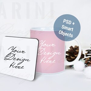 Puede incluir: Se muestra una taza rosa y un posavasos cuadrado blanco con el texto "Your Design Here". La taza está junto a un posavasos, piñas y pompones blancos. También hay un círculo azul con el texto "PSD + Smart Objects".